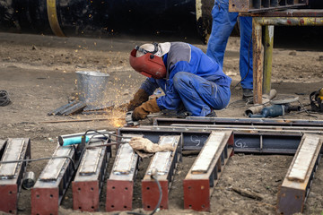 Worker grinds steel sections using angle grinder