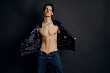 Male model in denim blue jeans and black leather jacket on black background
