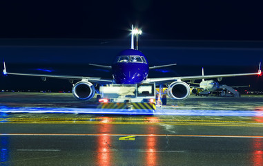 Closeup high detailed view on modern blue twin-engine passenger airplane taxiing at night by towing truck at international airport.
