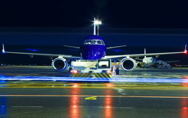 Closeup high detailed view on modern blue twin-engine passenger airplane taxiing at night by towing...