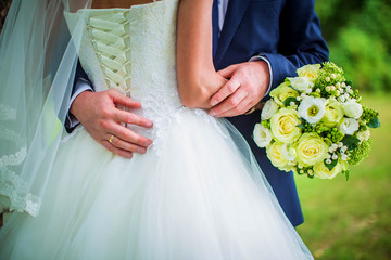 Bride holds bouquet and stands with her back, groom hugs her waist, closeup