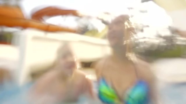 Two sisters fooling around in the pool, fighting and splashing.