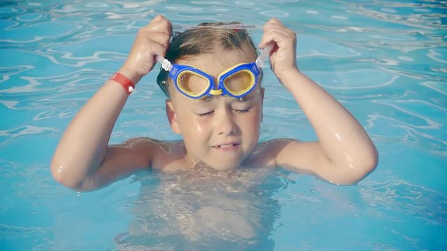 Little girl takes on a swimming goggles in a pool in summer.