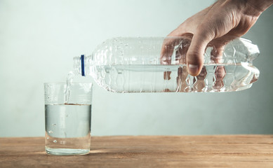 Man hand pours clean water from a bottle into a glass.
