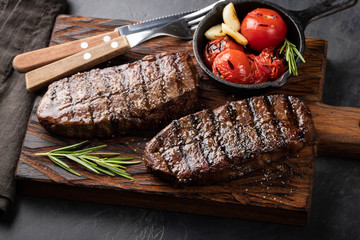 Closeup ready to eat steak Top Blade beef breeds of black Angus with grill tomato, garlic and on a wooden Board. The finished dish for dinner on a dark stone background. Top view