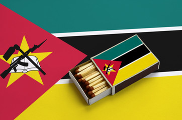 Mozambique flag  is shown in an open matchbox, which is filled with matches and lies on a large flag