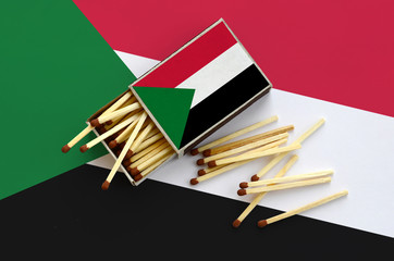 Sudan flag  is shown on an open matchbox, from which several matches fall and lies on a large flag