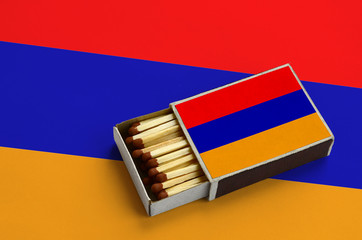 Armenia flag  is shown in an open matchbox, which is filled with matches and lies on a large flag