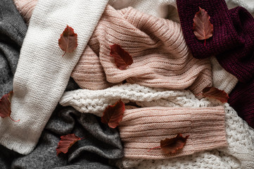 Background with warm sweaters. Pile of knitted clothes with autumn leaves, warm background,...