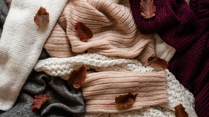 Background with warm sweaters. Pile of knitted clothes with autumn leaves, warm background, knitwear, space for text, Autumn winter concept. Copy Space.