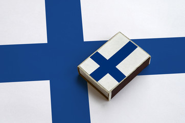 Finland flag  is pictured on a matchbox that lies on a large flag