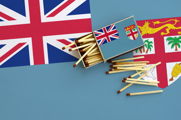 Fiji flag  is shown on an open matchbox, from which several matches fall and lies on a large flag