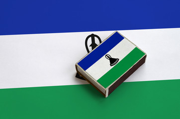 Lesotho flag  is pictured on a matchbox that lies on a large flag