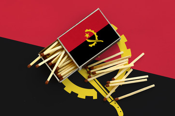 Angola flag  is shown on an open matchbox, from which several matches fall and lies on a large flag