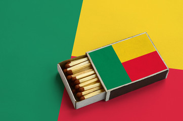Benin flag  is shown in an open matchbox, which is filled with matches and lies on a large flag