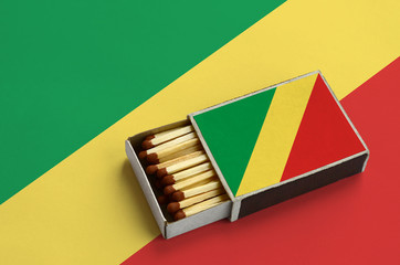 Congo flag  is shown in an open matchbox, which is filled with matches and lies on a large flag