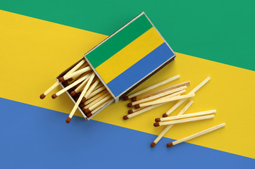 Gabon flag  is shown on an open matchbox, from which several matches fall and lies on a large flag