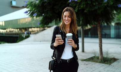 Young successful designer going to the office reading good news from friends on mobile phone and...