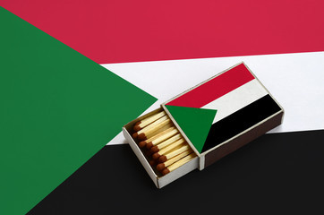 Sudan flag  is shown in an open matchbox, which is filled with matches and lies on a large flag