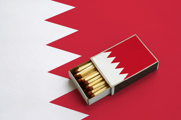 Bahrain flag  is shown in an open matchbox, which is filled with matches and lies on a large flag