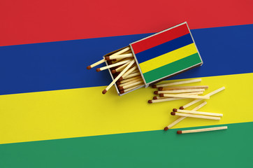 Mauritius flag  is shown on an open matchbox, from which several matches fall and lies on a large...