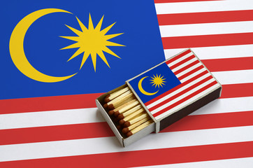 Malaysia flag  is shown in an open matchbox, which is filled with matches and lies on a large flag