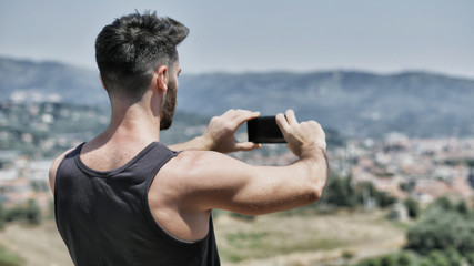 Young handsome man using smartphone to take shots and photos of the landscape at the seaside