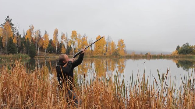Man makes a sweeping motion with a double barrel shot gun pointed in the sky as if he had a chance to make a shot but did not.