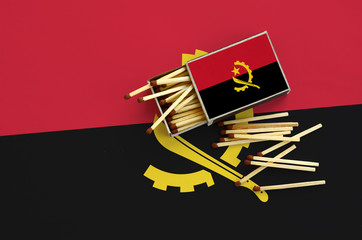 Angola flag  is shown on an open matchbox, from which several matches fall and lies on a large flag