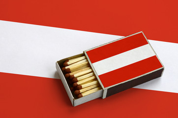 Austria flag  is shown in an open matchbox, which is filled with matches and lies on a large flag