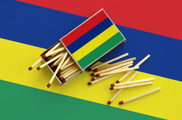 Mauritius flag  is shown on an open matchbox, from which several matches fall and lies on a large...