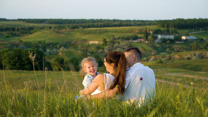 Fototapeta premium Pregnant couple with toddler daughter have leisure time outdoors back view. Happy young parents expecting baby with child at sunset. Parenthood, pregnancy, childhood, healthy, activity concept