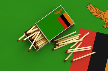Zambia flag  is shown on an open matchbox, from which several matches fall and lies on a large flag