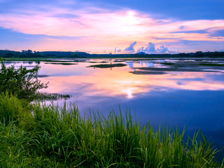 sunrise over big lake with reflection and green grass in foreground at Trad Thailand