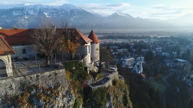 Drone shot flying past iconic Bled castle in Slovenia, with beautiful Winter landscape in the background