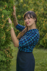 Landscape designer. Smiling beautiful brunette woman posing on green thuja trees background