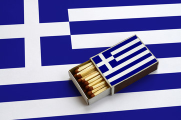 Greece flag  is shown in an open matchbox, which is filled with matches and lies on a large flag