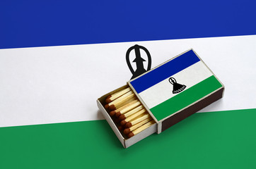 Lesotho flag  is shown in an open matchbox, which is filled with matches and lies on a large flag