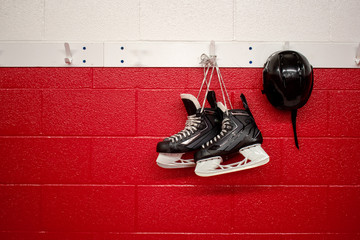 Hockey skates and helmet hanging in locker room with red background and copy 
