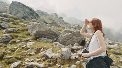 Naklejka premium A young woman hiker walks in the mountains with photo camera. Transfagarasan, Carpathian mountains in Romania