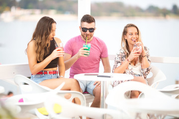 Three young friends in cafe near sea having good time and drinking cocktails