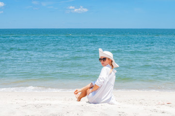 Fototapeta na wymiar Beautiful woman in hat sitting on the beach enjoying summer holidays