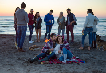 Fototapeta premium Couple enjoying with friends at sunset on the beach