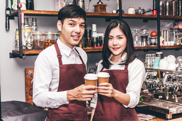 Portrait of couple small business owner smiling and holding cup of coffee behind the counter bar in a cafe