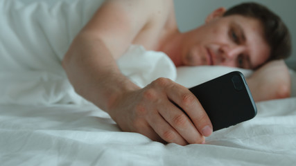 Young adult man lies on a bed and uses phone