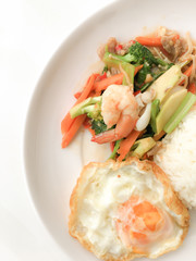 Fried Savory sauteed mixed vegetables with shimp and fried egg served with rice in white dish on white background as Thai homemade meal or recipe in the restaurant. Thai style food.