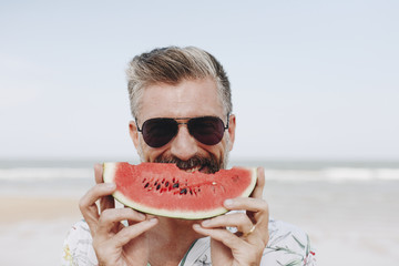 Mature man eating watermelon at the beach