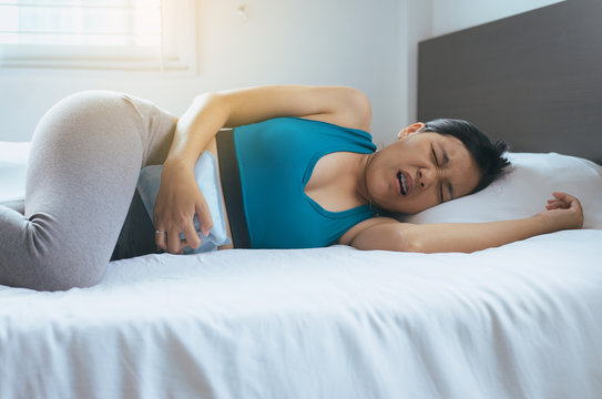Asian woman holding hot water bag on her stomach in bedroom,Female lying in bed