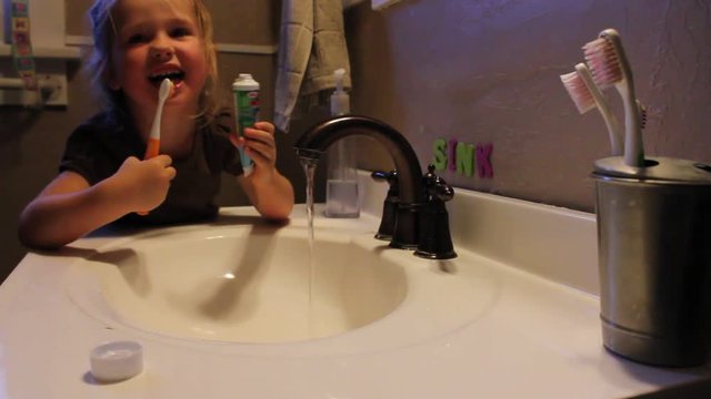 Young girl applies tooth paste to brush and brushes her teeth without help from adults.