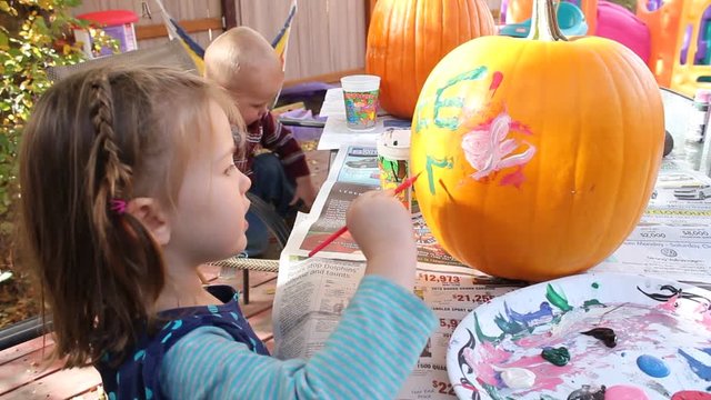 Two little kids painting jack-o-lanterns for Halloween. Close up of 3 year old painting the letter E on her pumpkin.